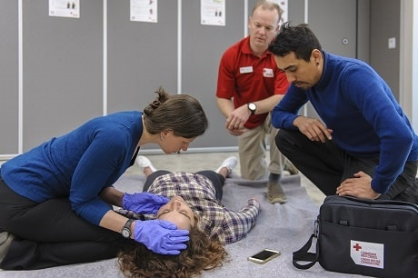 A group of people attending to a person lying on the floor

Description automatically generated